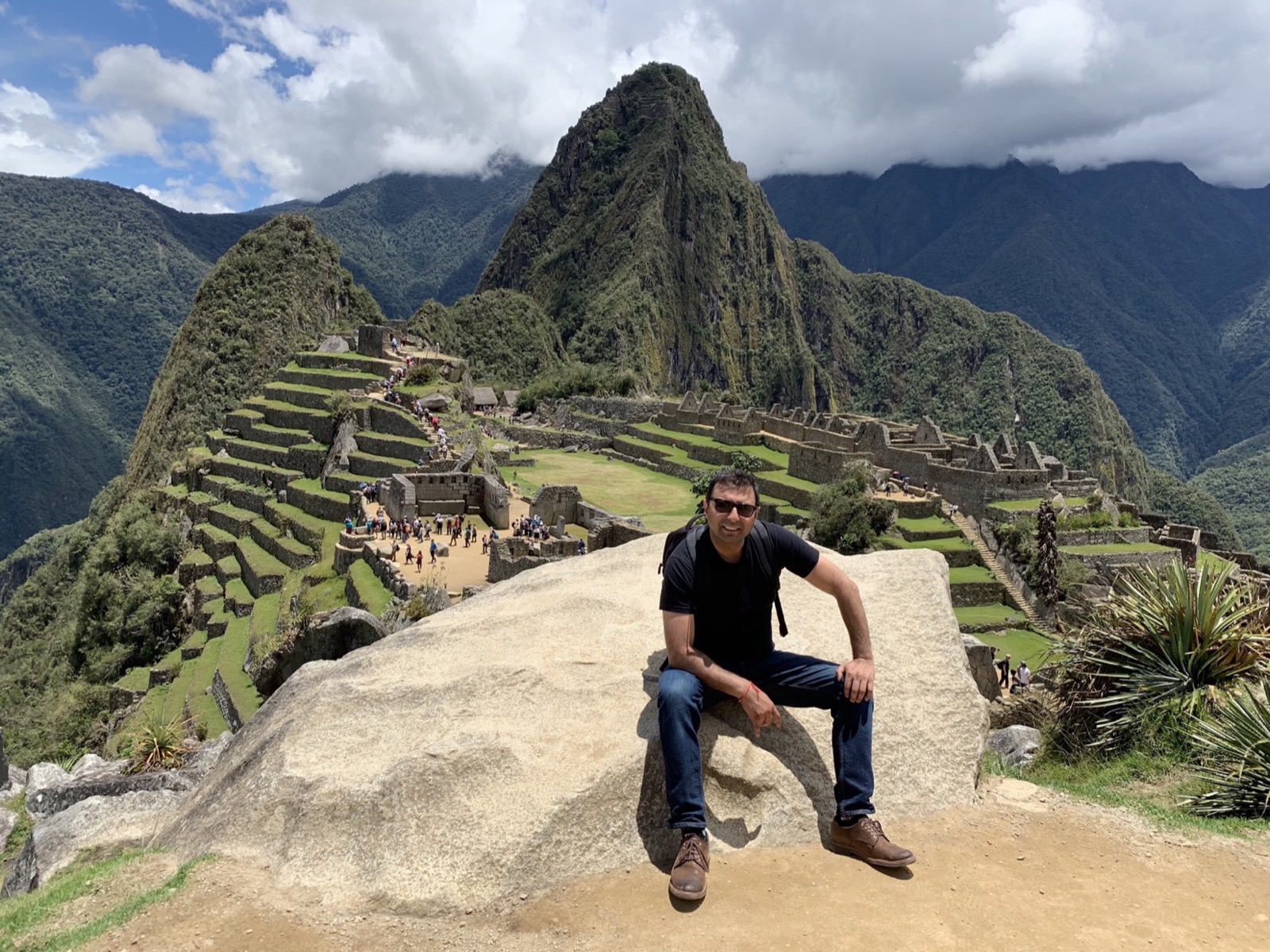 Karan M Gupta seated on a boulder in Peru, mountains and ancient stone terraces behind him
